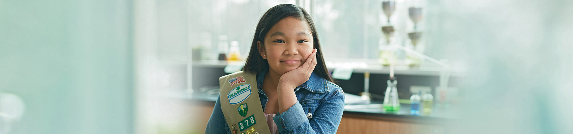  silver award girl scout wearing sash and pin sitting in classroom smiling with her chin resting on her hand 