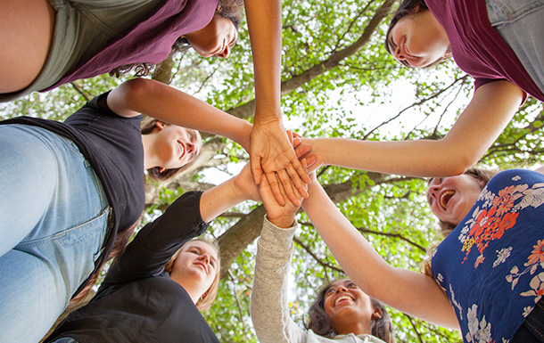 Group of girls standing in a circle and putting their hands in as a team under trees