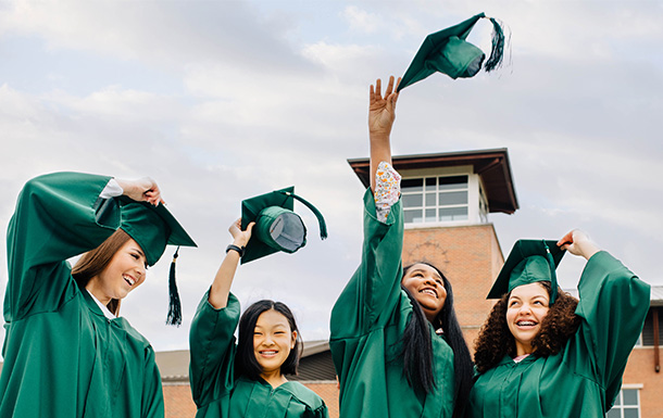 Teenage girls in graduation caps and gowns smiling and tossing their caps