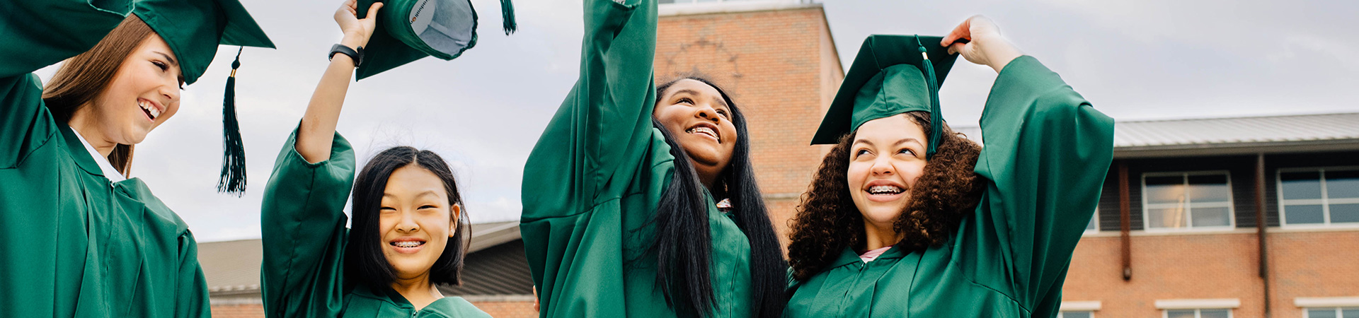  Girls in graduation caps and gowns smiling and tossing their caps together 