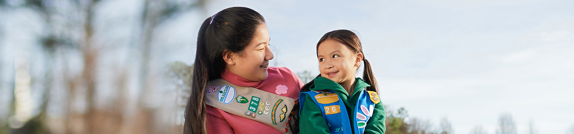  An older girl in uniform and a younger girl in uniform sit together and smile 