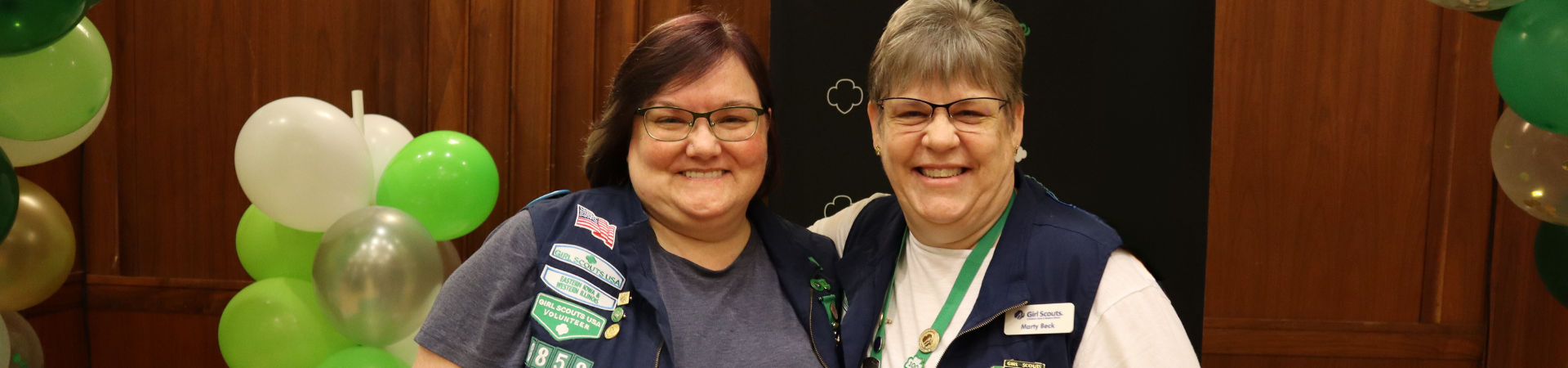  Two adult volunteers in official Girl Scout gear smiling together 