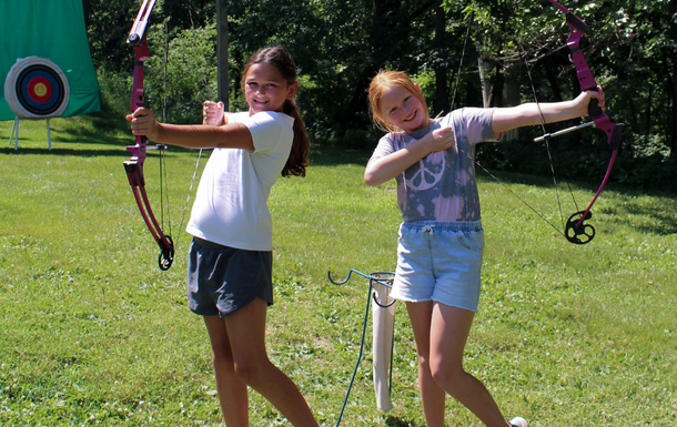 two girls smiling while holding bow and arrows